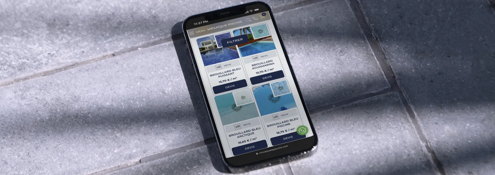 Smartphone on grey stone tiles displaying the Mosaïque Piscine online pool mosaic catalogue